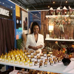 SKNMUSE Owner, Ezinne Tracey Iroanya-Adeoye posing behind a table containing her skin care products.
