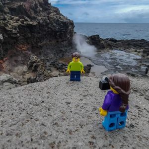Two LEGO characters shown on a rock on a beach.