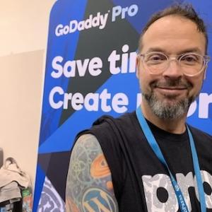 Adam Warner standing in front of a GoDaddy banner.
