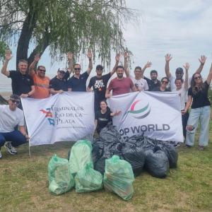 DP World team members in Argentina participate in a beach clean-up, standing behind collected waste and holding DP World and Terminales Río de la Plata banners.