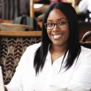 African American female, smiling, at work behind a laptop.