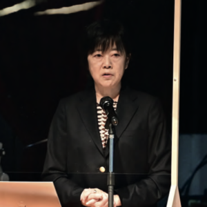 Japanese Aflac employee speaking at a podium.