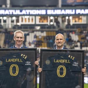 Two people holding up soccer jerseys with the words "Landfill 0"