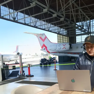 Alejandro working in an airplane hanger with a laptop.