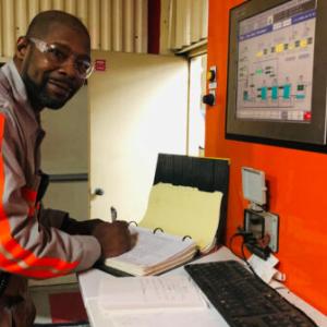 a person writing in a records book on a desk with monitors on the wall