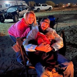 Amber shown with her husband and child at a campfire.