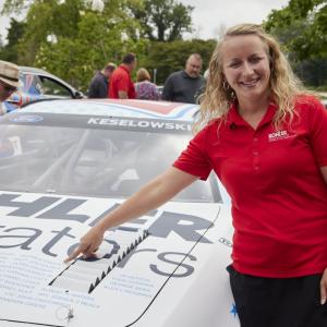 a person stands by a car and points to a name on the hood
