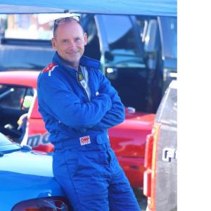 Andy O'Brien in a race suit, leaning on a car.