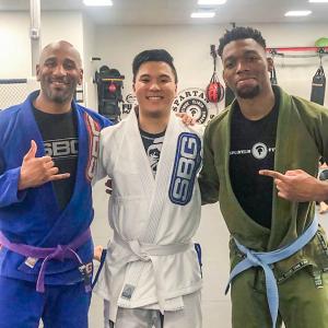 Three people wearing martial arts suits with their arms around each other
