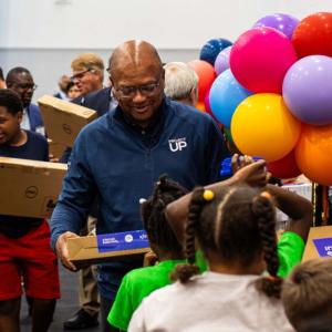 Broderick D. Johnson handing new laptops to children.