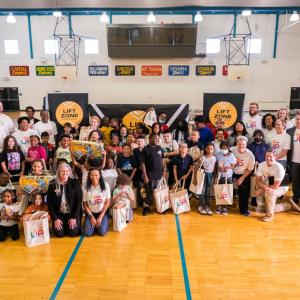 a large group of students and adults in a gym, most are wearing "Project UP" t-shirts and holding tote bags