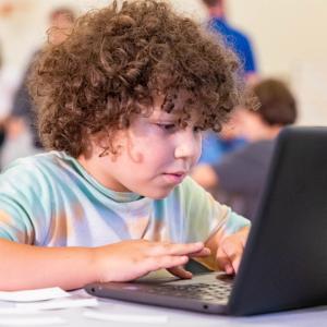 a child engaged on a laptop, others blurred behind him