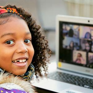 Young black student seated in front of a laptop smiling.