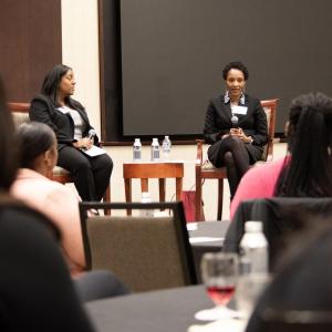 Two speakers seated on a stage in front of a room of others