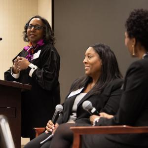 A speaker at a podium looking over to two others seated to the side