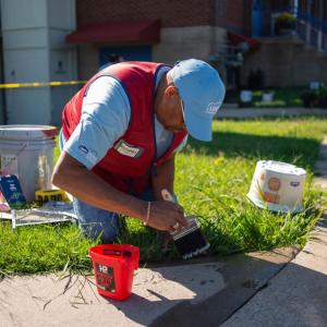 Photo of man sitting in a patch of grass, painting a sidewalk