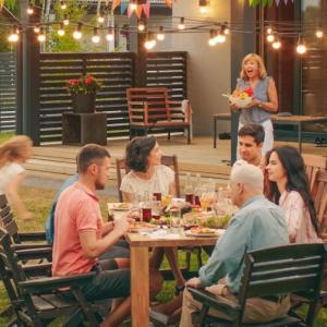 group of people sitting at an outside dining table, children running in the background