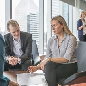 group of three people sitting around a small table looking at the same document