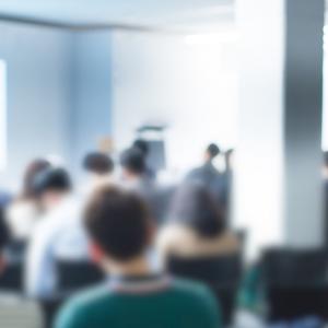 blurry representation of a speaker on a podium in front of audience