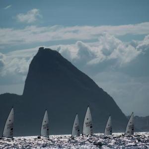 sailboats in the water in front of a dramatic mountain with clouds in the distance