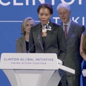 Didi Bertrand Farmer at a podium, The Clintons behind her.