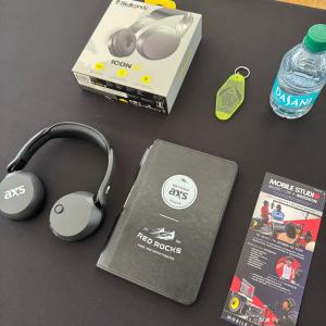 AXS-branded headphones, a Skullcandy headphone box, Beyond AXS at Red Rocks materials and a Mobile Studio on a Mission brochure arranged on a table.