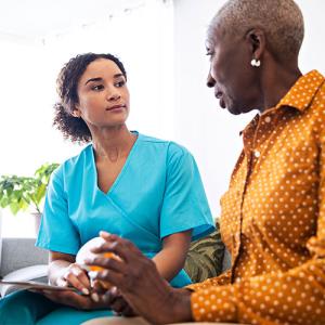 A person in scrubs and a patient sitting next to each other, looking at the other.