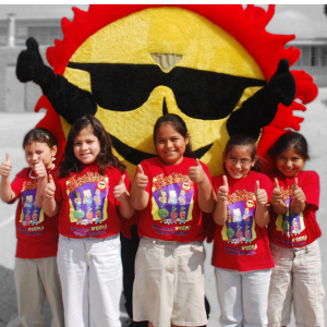 Five children in matching t-shirts give 'thumbs-up'. A Bienstar mascot behind them.