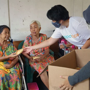 Two volunteers handing out food to two elderly people in chairs
