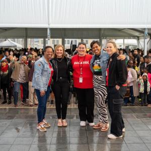 Five people standing together in front of cheering crowd