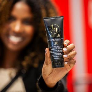 A smiling person holding a bottle of sunscreen