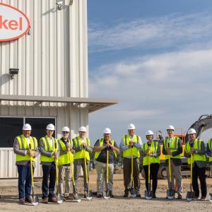 Group of ten people in hi-visibility vests holding shovels in front of new Henkel facility