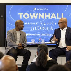 Two people seated on a small stage, a display with "Townhall Digital Equity Georgia" and comcast logo  behind them. A small audience seated in front.