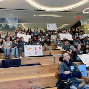 Bleachers with many students seated, holding signs.