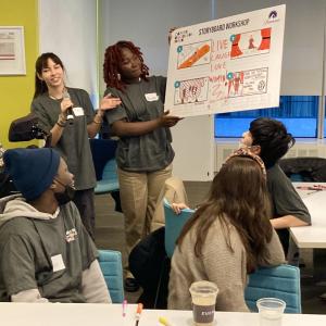 Two students present their 'Storyboard Workshop' to a room of others seated.