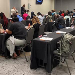 People sat at rows of tables and chairs at an event 
