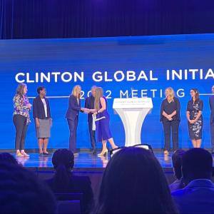Image of eight people on stage in front of a backdrop that says, "Clinton Global Initiative"
