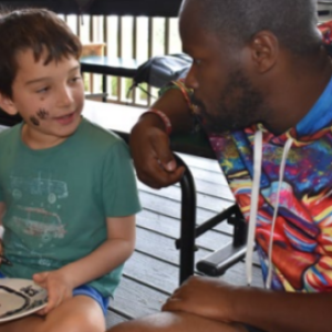 An adult talking with a smiling child who is drawing.