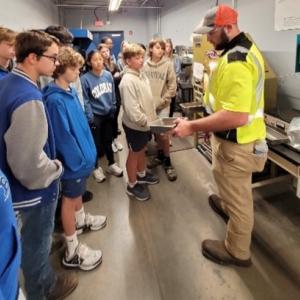 A volunteer in safety uniform showing something to a group of kids.
