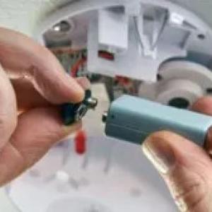 Close up of someone connecting a battery to a CO2 detector.