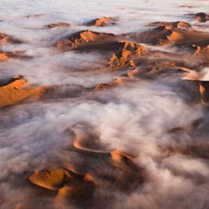 Panoramic landscape of low clouds over desert sands and hills.