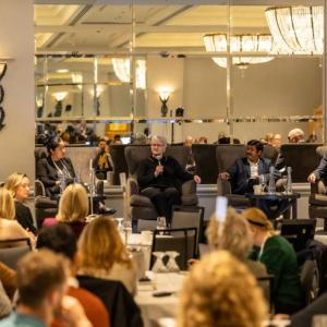 A panel of five people speaking and answering questions at a conference event, seated on stage in front of an audience.