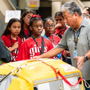 An adult showing a group of children an airplane part.
