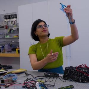 A person in a workshop, holding up some blue wire
