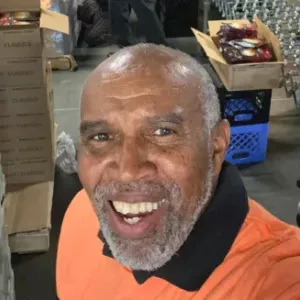 Calvin taking a selfie next to pallets of canned foods in a storage room.