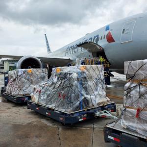 Three pallets of cargo in line as one is loaded into a plane with "American Airlines" on it.