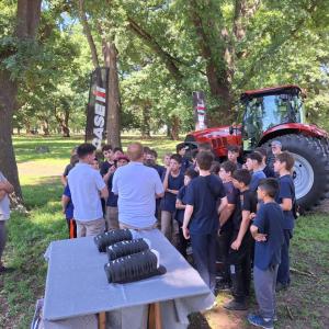 Two adults speaking to a group of students with a tractor behind them