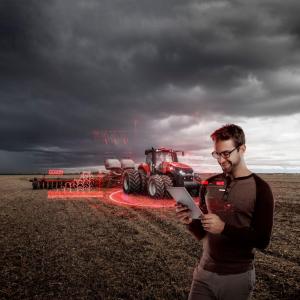 Red agricultural equipment in a crop field, with a person stood looking at a tablet PC