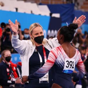 Cici and Simone Biles with arms out for a hug, reporters and spectators around them