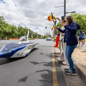 People cheering at the side of the road as a solar car drives past